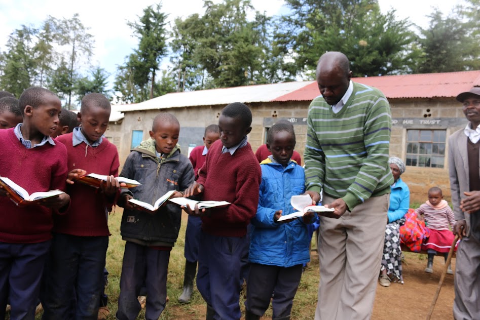 Displaying MEKARO PS DEPUTY HEAD TEACHER HELPING PUPILS OUT WITH OPENING A BIBLE VERSE.JPG